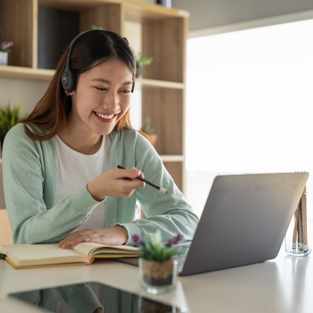 Mujer joven sonriendo en una videollamada de estudio con auriculares, sugiriendo apoyo y aprendizaje online.